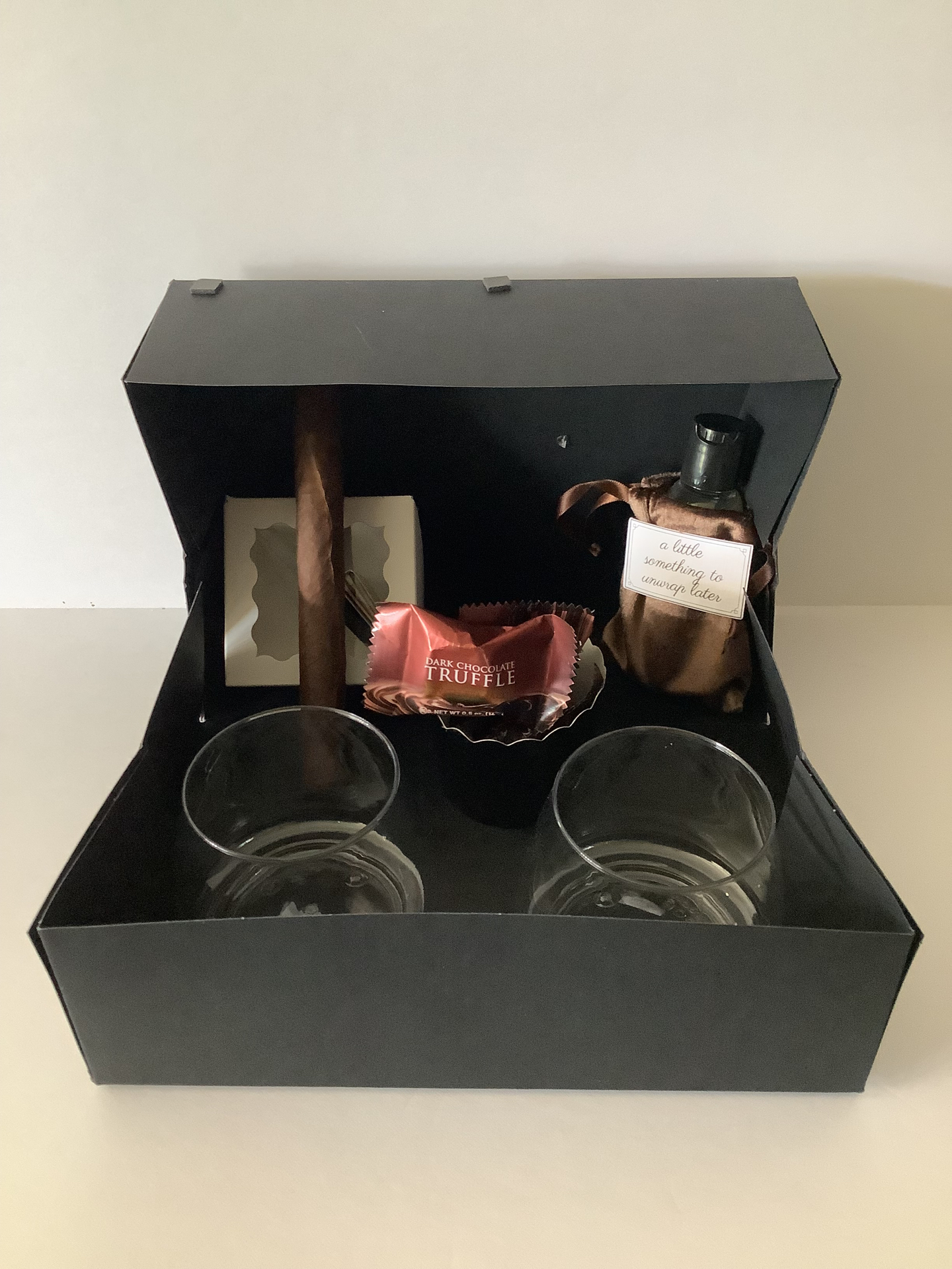 Open gift box with cigar, cologne, truffle, and rocks glasses